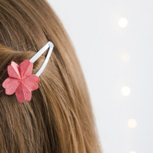 Eine dunkelblaue Frau trägt in ihren Haaren eine weiße Haarspange die mit einer Origami Kirschblüte verziert ist.