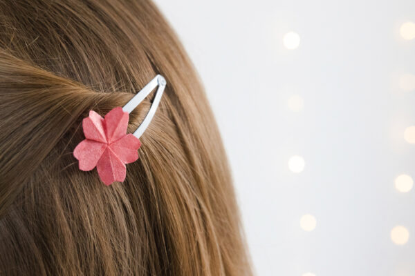 Eine dunkelblaue Frau trägt in ihren Haaren eine weiße Haarspange die mit einer Origami Kirschblüte verziert ist.