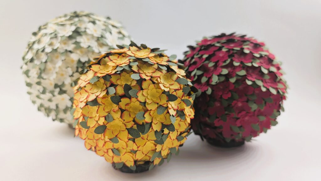 3 Beispiele für Blumenkugeln aus Papier in rot, gelb und Creme.